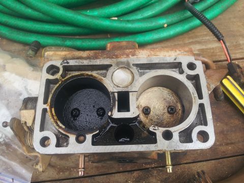 1988 Ford Bronco - Close-up of a carburetor, showing two throttle plates. One plate is clean, while the other is covered in dark residue.