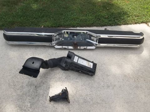 1995 Ford Bronco - Vehicle parts, including a chrome bumper and air intake system, are laid out on a concrete surface.