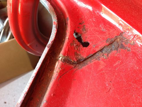 1964 Ford Fairlane - Close-up of a red car door edge revealing significant rust damage and a small hole.