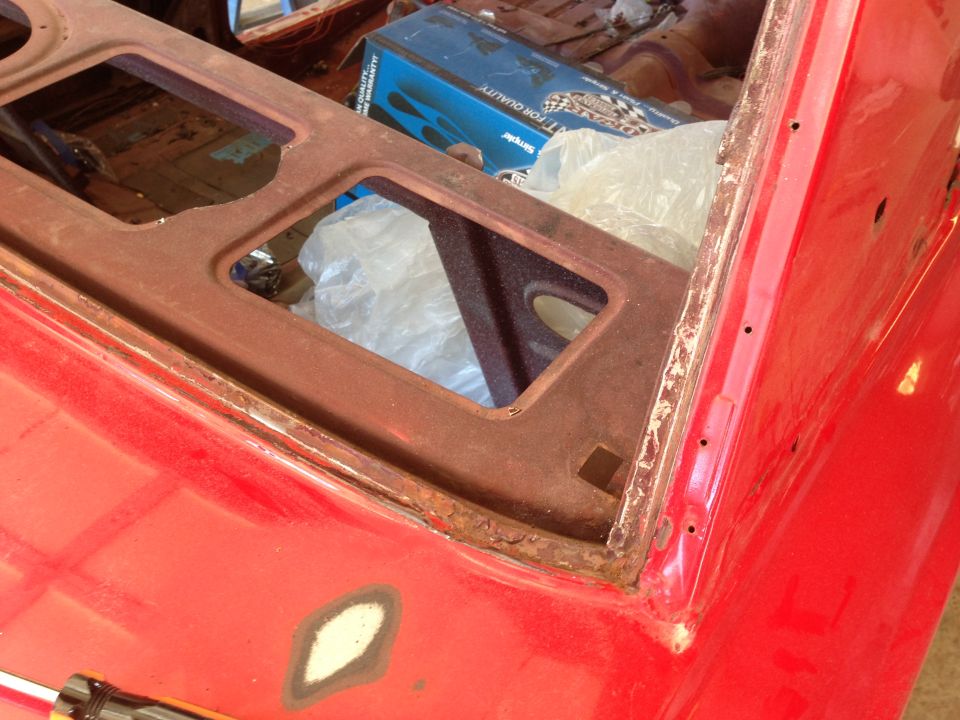 Close-up of red car body panel showing rust around window frame and primer spots