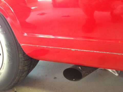 1964 Ford Fairlane - Close-up of a red vehicle's lower body panel, showing wear and an exhaust pipe.