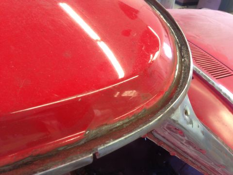 1964 Ford Fairlane - Close-up of a red car's body panel, showing unfinished seams and trim, with another vehicle in the background.