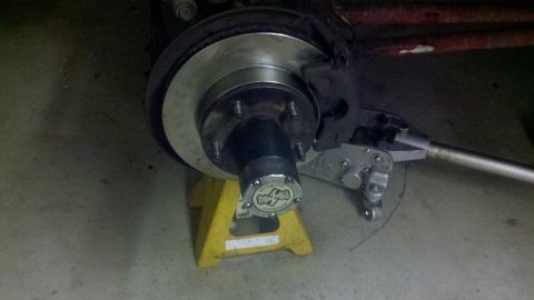 1992 Ford Bronco - Detail of a vehicle's wheel hub and brake assembly, supported by a yellow jack stand. The hub cap features visible text and a logo.