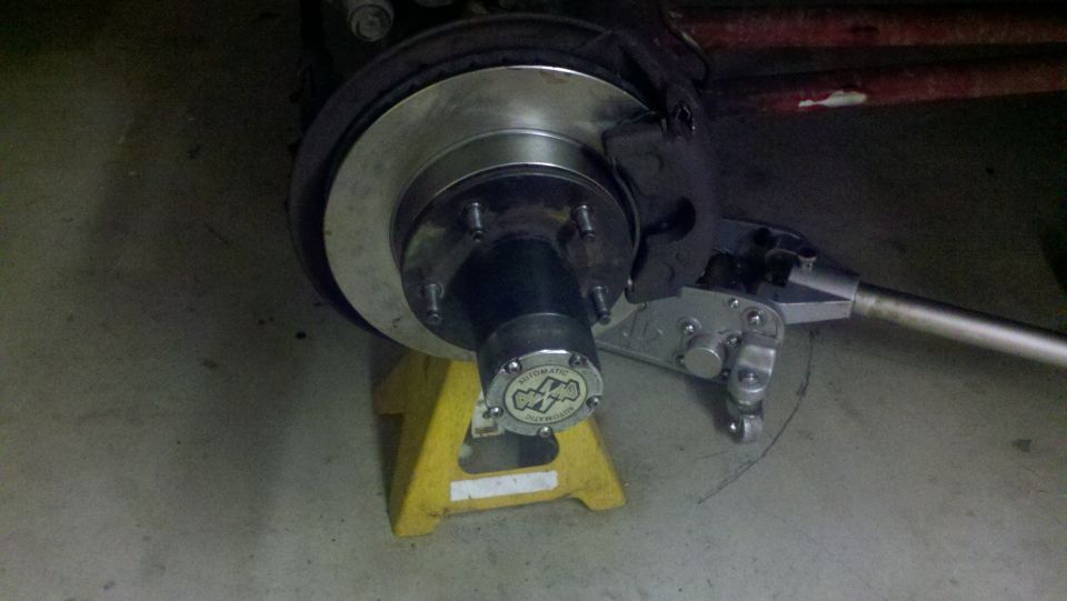 Close-up of a wheel hub with a yellow jack stand and part of a brake assembly. Hub cap has text and a logo