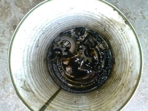 1992 Ford Bronco - Gears submerged in dark oil inside a white bucket, with a Supermotors.net logo visible.