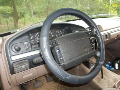1995 Ford Bronco - The interior of a Ford Bronco shows a tan dashboard and a dark steering wheel cover.