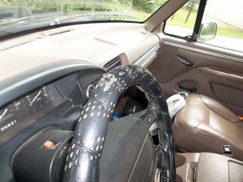 1995 Ford Bronco - The interior of a vehicle shows a tan dashboard, brown seats, and a worn steering wheel cover.