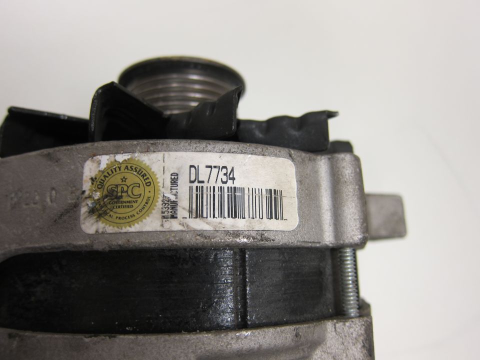 Close-up of an alternator part with a label that reads DL7734 and a SPC Quality Assured Government Certified seal