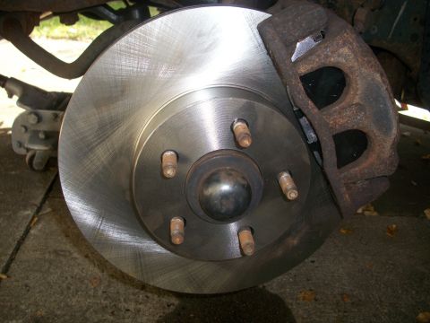 2001 Ford Crown Victoria - Close-up of a vehicle's brake rotor and caliper assembly, showing a new rotor and a rusty caliper.