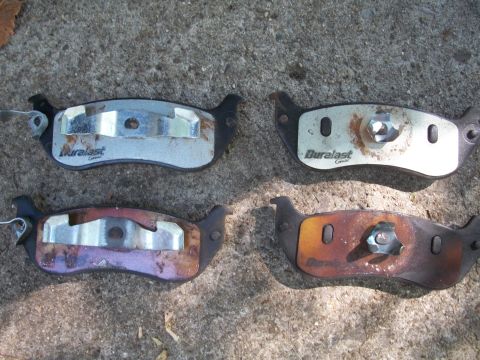 2001 Ford Crown Victoria - Four Duralast brake pads are laid out on a rough concrete surface, showing signs of wear and rust.