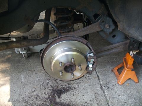 2001 Ford Crown Victoria - Close-up view of a vehicle's rear brake rotor and caliper, with the car elevated on a jack stand.