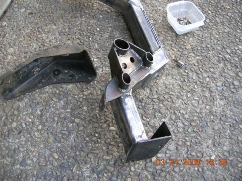 1995 Ford Bronco - A fabricated steel part, possibly an engine crossmember, lies on a gravel surface next to a separate metal bracket.