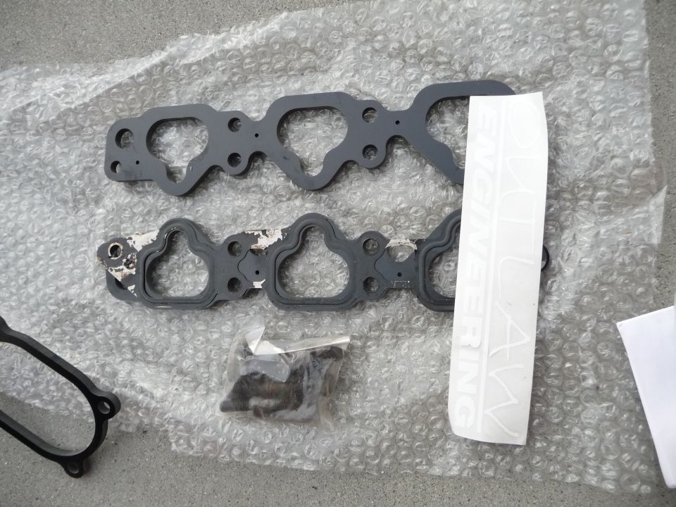 Engine intake manifold gaskets and a bag of hardware on bubble wrap. White sticker with text is visible