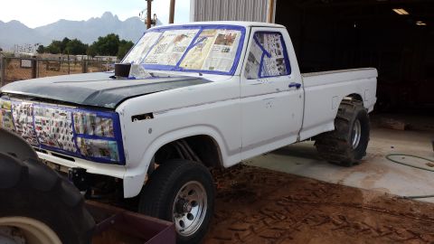 1995 Ford Bronco - This white pickup truck, likely from the early 1980s, is being prepped for paint with its grille and windows taped off.
