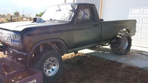 1995 Ford Bronco - Pickup truck with custom modifications, including large rear tires and a hood scoop, parked in front of a garage.