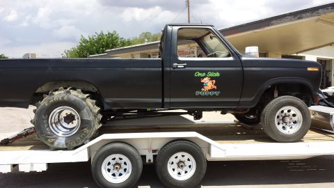 1995 Ford Bronco - A black pickup truck with large rear tires is being transported on a trailer.