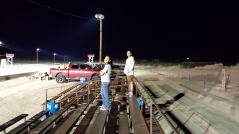 1995 Ford Bronco - A red pickup truck is parked on a dirt track at night, illuminated by stadium lights.