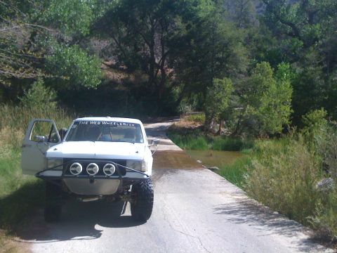 1990 Ford Bronco - Photo of a white off-road truck stopped at a tree-lined creek crossing, not a technical document.