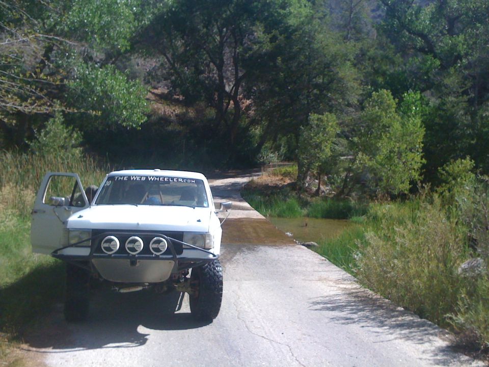 White off-road truck parked on a road by a creek crossing