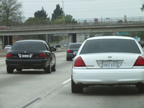 2003 Ford Crown Victoria - Photo of a white Crown Victoria and black sedan on a freeway beneath an overpass, not a technical document.