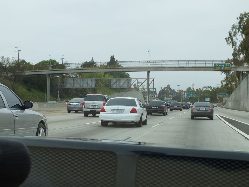 Traffic on multi-lane freeway with pedestrian bridge and Downey Rd sign