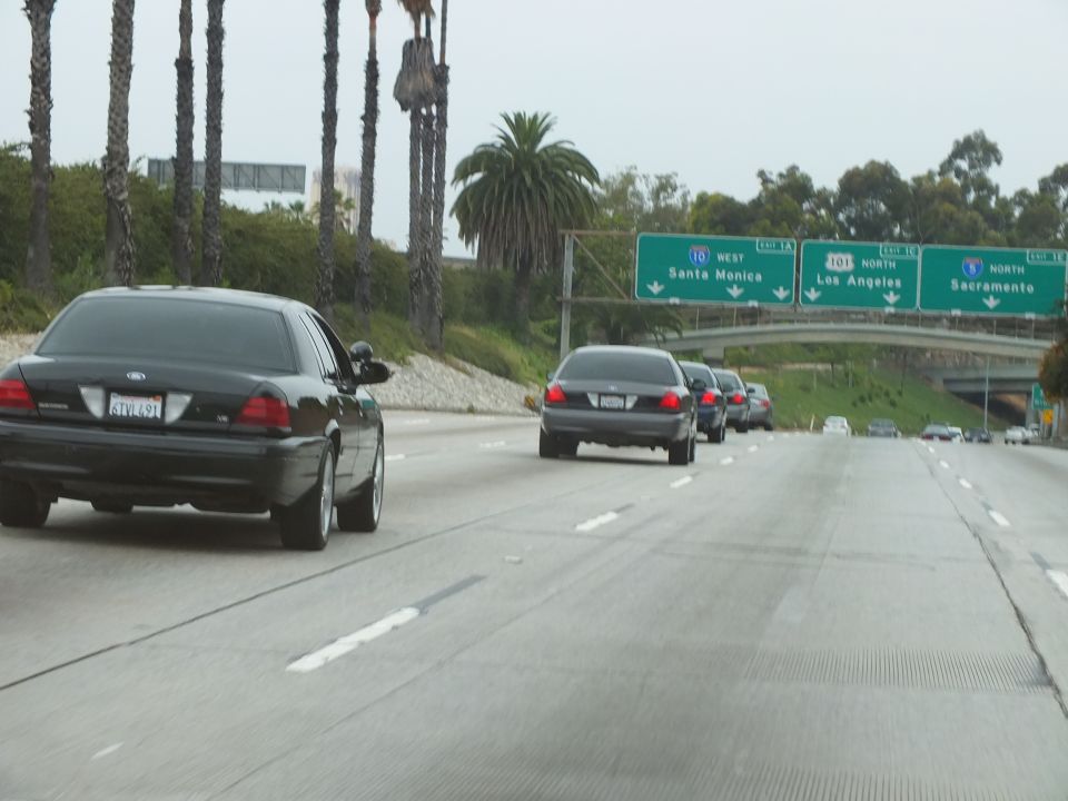 Black sedans on a freeway near green signs for Santa Monica, Los Angeles and Sacramento