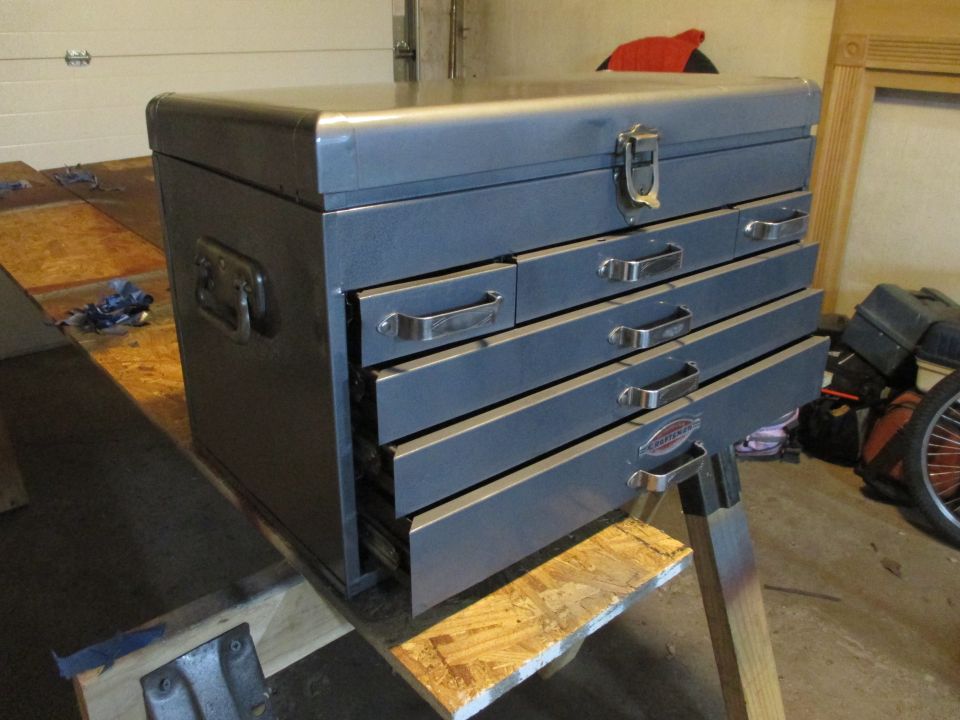 Gray metal toolbox with five drawers and a latch on top, resting on a wooden surface