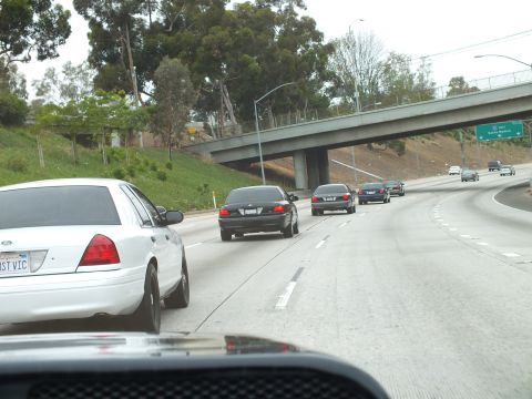 2003 Ford Crown Victoria - Photo of a white Crown Victoria and dark sedans on a curving freeway near an overpass, not a technical document.
