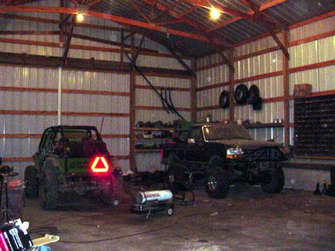 1992 Ford Bronco - Two off-road vehicles are parked inside a barn, one with a prominent triangular taillight.