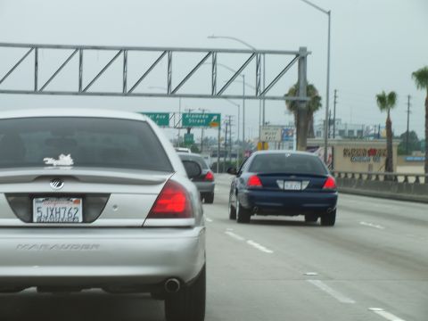 2003 Ford Crown Victoria - Photo of a silver Mercury Marauder and blue sedan on a freeway beneath a sign gantry, not a technical document.