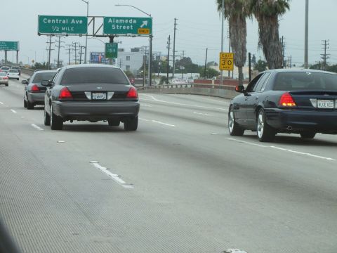 2003 Ford Crown Victoria - Photo of dark Crown Victoria sedans on a freeway beneath Central Ave and Alameda Street signs, not a technical document.