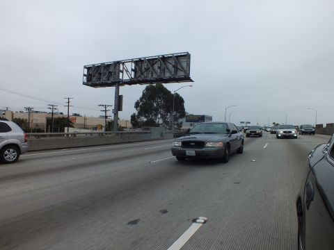 2003 Ford Crown Victoria - Photo of a gray Crown Victoria and cars on a freeway under an empty billboard frame, not a technical document.