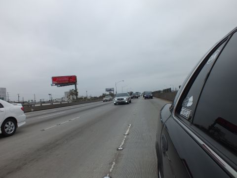 2003 Ford Crown Victoria - Photograph of multilane freeway traffic on a gray day, taken from inside a dark sedan with a roadside billboard visible.