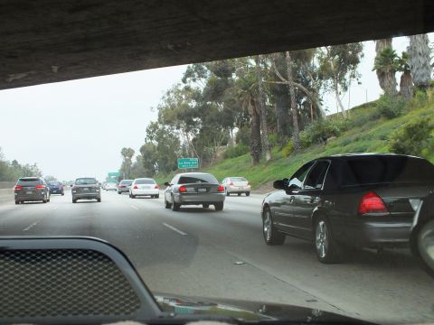 2003 Ford Crown Victoria - Photograph of freeway traffic viewed from beneath an overpass beside a green hillside.