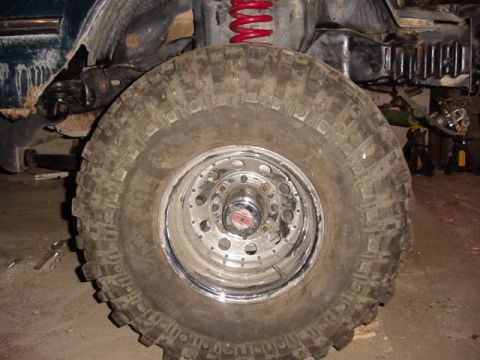 1992 Ford Bronco - Close-up of a large off-road tire and suspension components of a vehicle in a garage.
