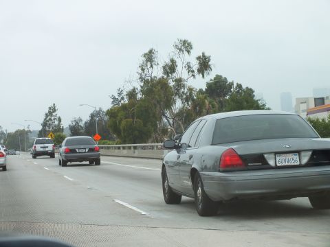 2003 Ford Crown Victoria - Photograph of a gray Crown Victoria sedan in freeway traffic beside a guardrail and trees.
