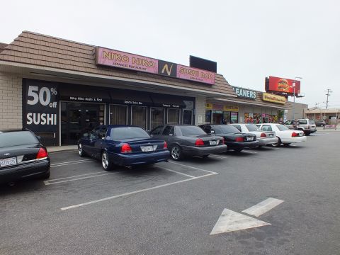 2003 Ford Crown Victoria - Photograph of sedans parked in front of the Niko Niko Sushi Bar strip mall with a 50% off sushi sign.