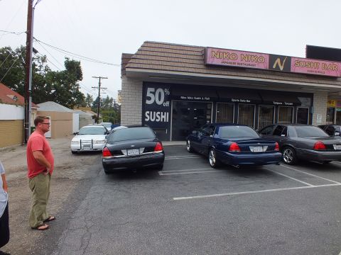 2003 Ford Crown Victoria - Photograph of a man standing near sedans parked at the Niko Niko Sushi Bar strip mall.