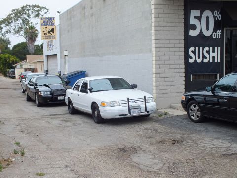 2003 Ford Crown Victoria - Photo of Ford Crown Victoria sedans parked along a brick wall near an auto repair shop.