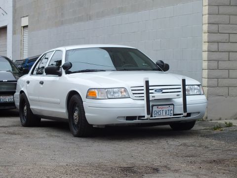 2003 Ford Crown Victoria - Photo of a white Ford Crown Victoria with push bar and GHST VIC plate parked by a wall.
