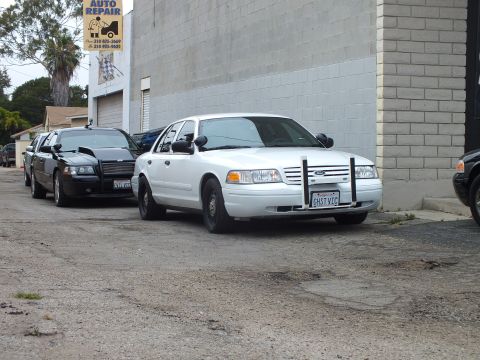 2003 Ford Crown Victoria - Photo of white and black Ford Crown Victoria sedans parked in an alley near an auto repair sign.