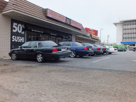 2003 Ford Crown Victoria - Photo of a row of Ford Crown Victoria sedans parked in front of a strip mall sushi bar.