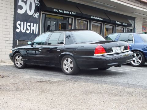 2003 Ford Crown Victoria - Photo of a black Ford Crown Victoria parked outside a sushi restaurant storefront.