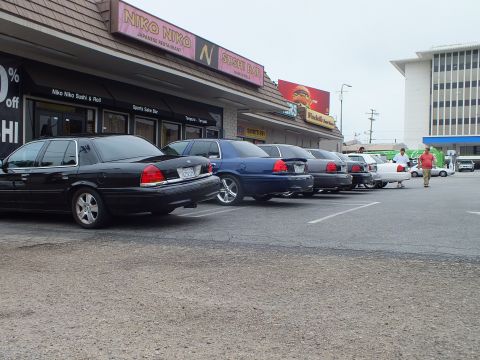2003 Ford Crown Victoria - Photo of a row of Ford Crown Victoria sedans parked outside a strip mall sushi bar.