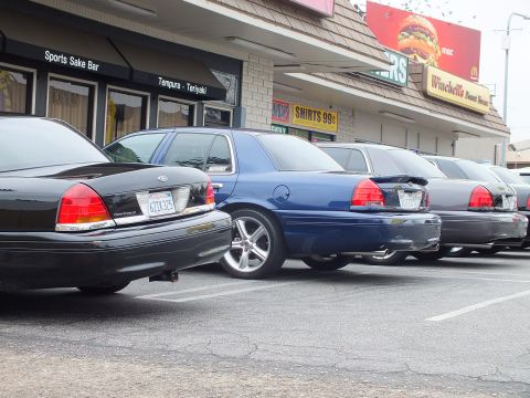 2003 Ford Crown Victoria - Photo of black and blue Ford Crown Victoria sedans parked outside strip mall shops.