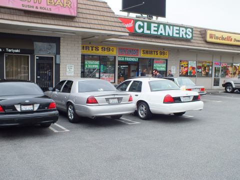 2003 Ford Crown Victoria - Photo of black, silver and white Ford Crown Victoria sedans parked outside strip mall shops.