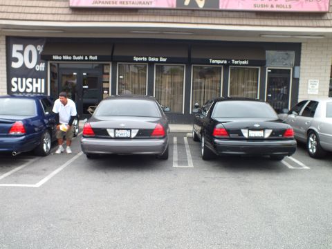 2003 Ford Crown Victoria - Photo of Ford Crown Victoria sedans parked in front of a sushi restaurant storefront.