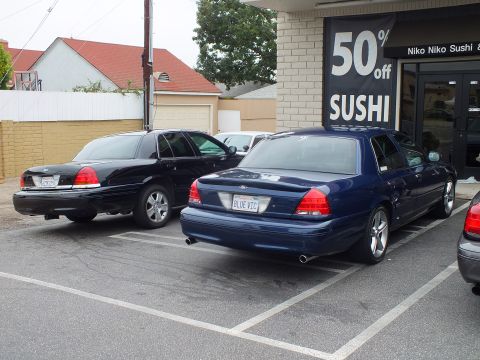 2003 Ford Crown Victoria - Photo of blue and black Ford Crown Victoria sedans parked outside a sushi restaurant.
