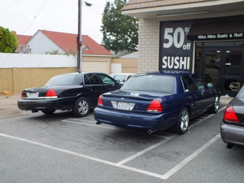 2003 Ford Crown Victoria - Photo of blue and black Ford Crown Victoria sedans parked in front of a sushi restaurant.