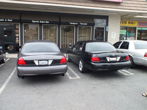 2003 Ford Crown Victoria - Photo of gray and black Ford Crown Victoria sedans parked outside strip mall storefronts.